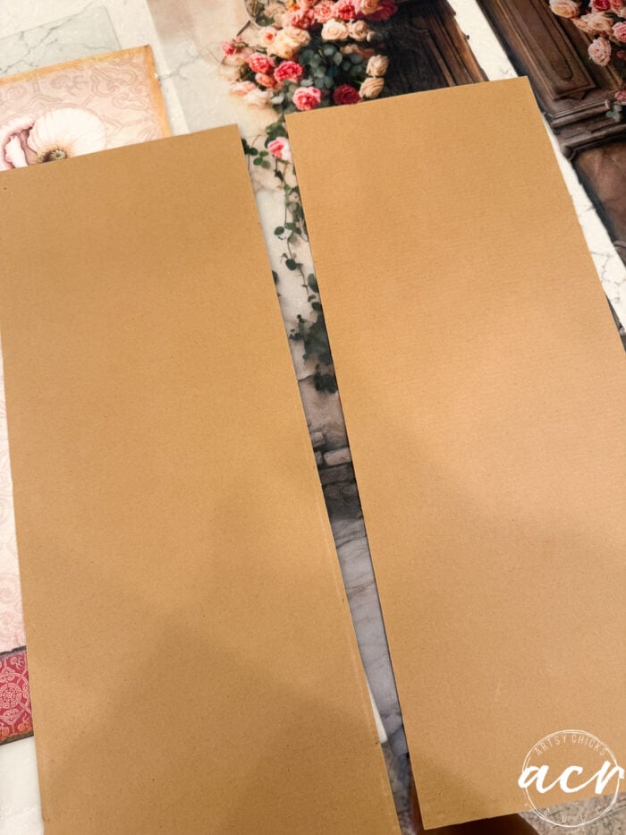 Two rectangular sheets of plain brown cardstock rest atop floral and decorative patterned papers, evoking the delicate layering of tissue paper. A small circular watermark with the letters acm is in the lower right corner.