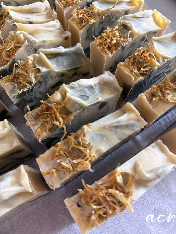 Several handcrafted natural fall soaps with marbled gray and cream colors are arranged together. The tops of these all natural soaps are textured and decorated with dried yellow flower petals. The corner of the image features a copyright watermark.