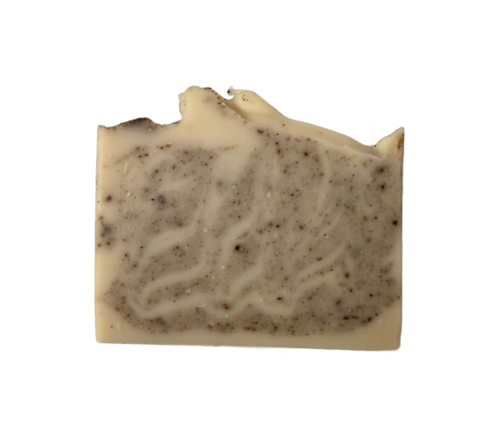 A rectangular bar of handmade natural soap with a rough top edge, beige in color and speckled with dark brown flecks, is shown on a white background.