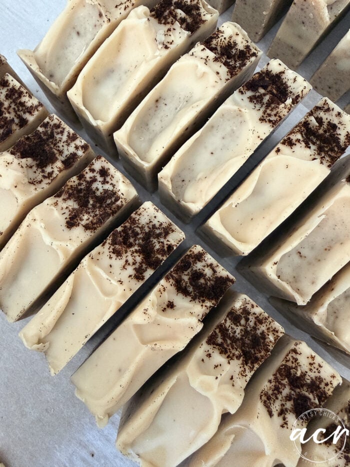 Rows of handmade Natural Fall Soaps with a creamy beige color, swirled tops, and a sprinkle of dark brown powder on each. The soap bars are neatly arranged on a white surface.
