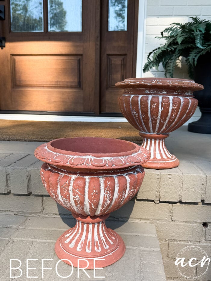 Two terracotta-colored decorative urn planters with white distressed detailing, styled like DIY concrete planters, sitting on front porch steps.