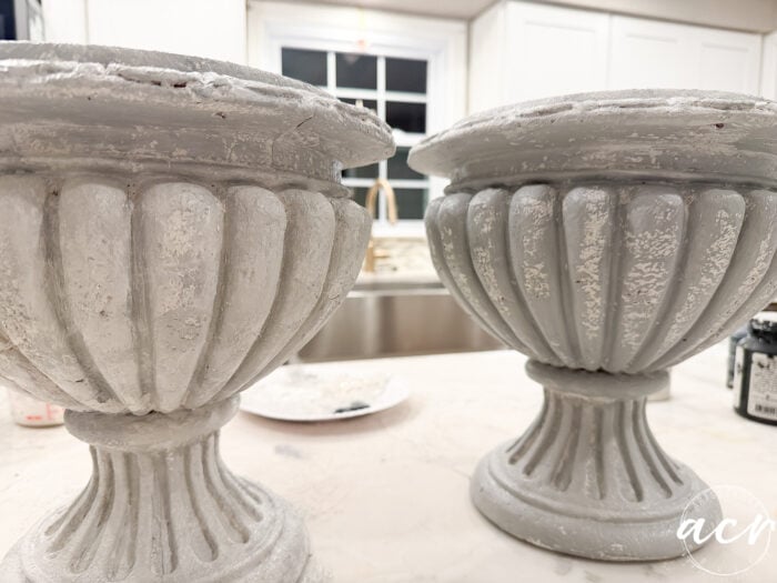 Two fluted, grey faux concrete urn-shaped planters with a distressed finish sitting on a countertop.