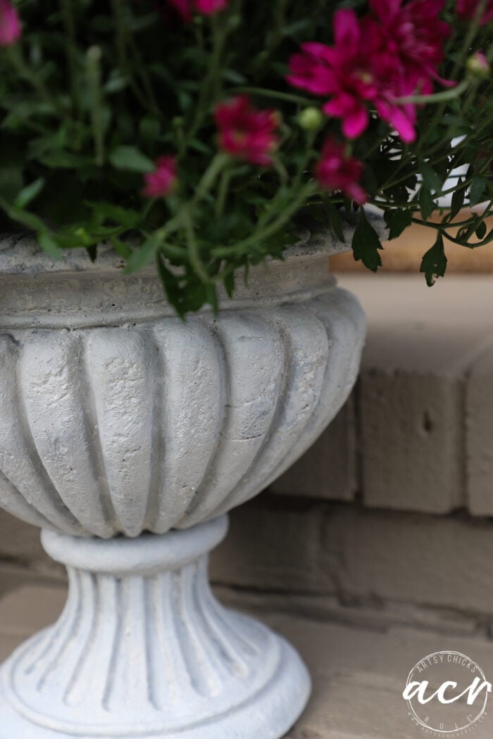 A decorative, pale gray DIY concrete planter filled with magenta flowers.