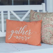 Our Simple Fall Porch Two decorative pillows on a white wooden bench for simple fall decor; one is orange with the word gather embroidered on it, and the other has a tan and orange paisley pattern.