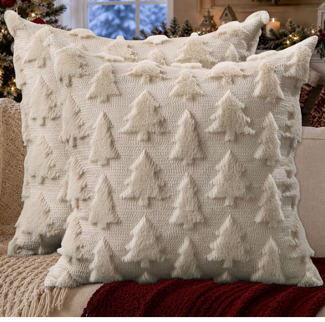 Two cream-colored throw pillows with a textured, raised Christmas tree pattern resting on a sofa as part of our holiday picks.